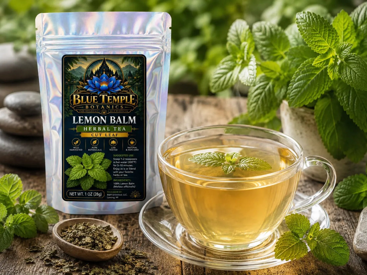 A Blue Temple Botany Lemon Balm Herbal Tea pouch next to a glass cup of brewed lemon balm tea on a wooden surface with fresh mint leaves and loose tea.