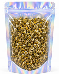 A clear, resealable stand-up pouch with an iridescent holographic finish, filled with dried small white and yellow flowers, shown on a plain white background.